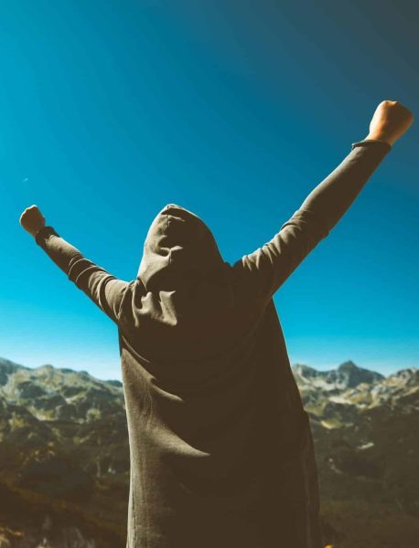 Victorious female person standing on mountain top with arms raised in V. Winning and success. Achievement and accomplishment in life. Toned image.